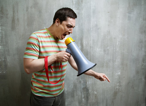 man yells into a megaphone and points down on the gray textured