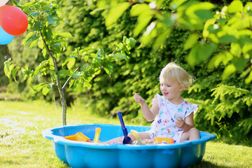 Happy little girl playing in sandbox in the garden