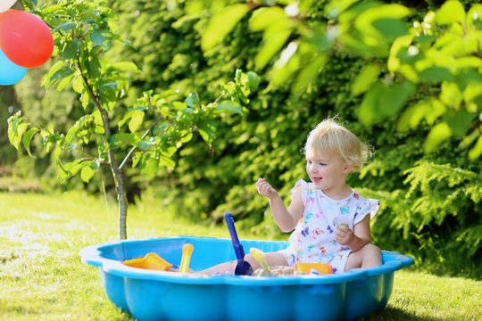 Happy little girl playing in sandbox in the garden