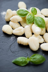 Raw gnocchi with green basil leaves, close-up, vertical shot