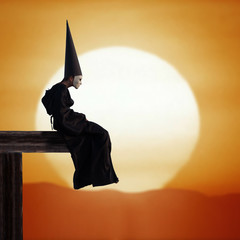 Strange person in black cloak and dunce hat at sunset