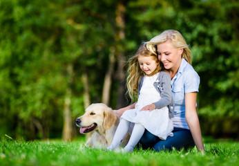 Mother and daughter with labrador sitting on the green grass