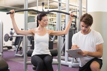 Fit brunette using weights machine for arms with trainer taking