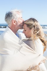 Fototapeta premium Affectionate couple wrapped up in blanket on the beach