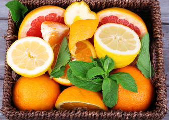 Obraz na płótnie Canvas Fresh citrus fruits with green leaves in wicker basket