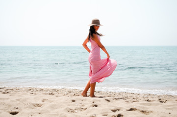 Beautiful woman with long pink dress and sun hat on a tropical b