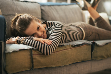 Smiling young woman laying on divan in loft apartment