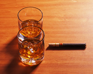 Highball whiskey glass with ice and cigar on wooden background.