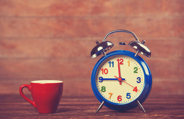 Cup of coffee and alarm clock on wooden table.