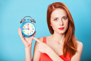 Surprised redhead women woth alarm clock on blue background.