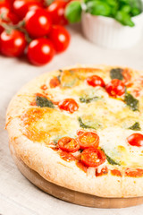 Home made pizza on wooden board with tomatoes on background