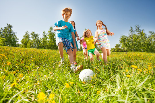 Happy Kids Playing Football In Green Field