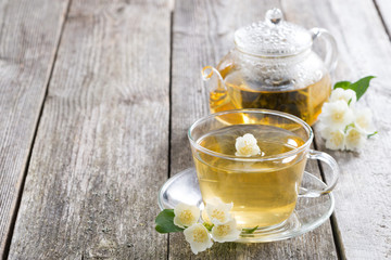 kettle and a cup of green tea with jasmine on wooden background