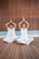 Fototapeta na wymiar Attractive couple in white sitting in lotus pose with hands toge