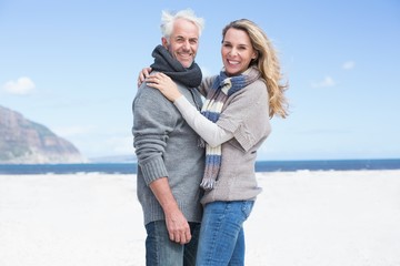 Smiling couple looking at camera on the beach in warm clothing