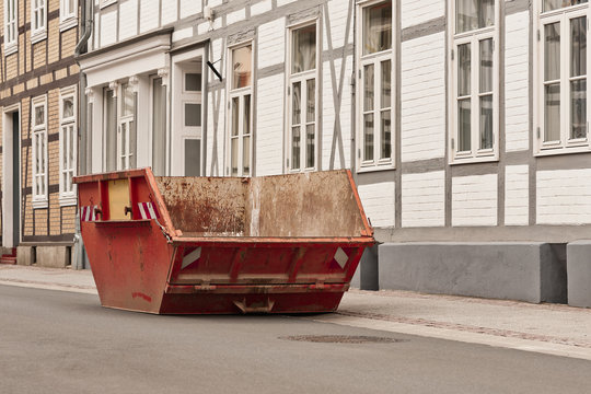 Ein leerer roter Bauschuttcontainer vor einem Fachwerkhaus