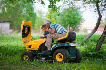 Grandfather and grandson at sunset checking lawn mower