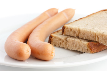 Two cooked frankfurter sausages on a plate with bread