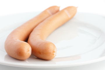 Two cooked frankfurter sausages on a plate with white background