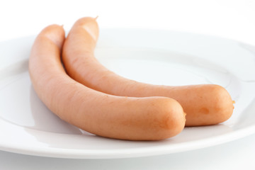 Two cooked frankfurter sausages on a plate with white background
