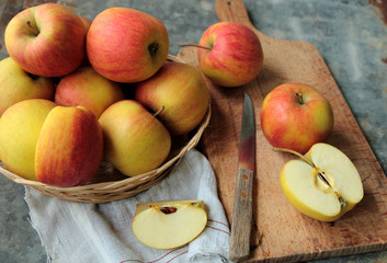 Red apples in a wicker and sliced fruit on a cutting board