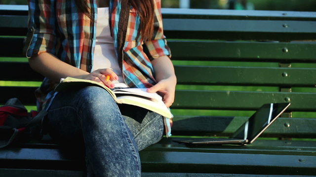Young student doing homework with laptop and notebook in the par