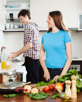 woman cooking food while man washing dishes