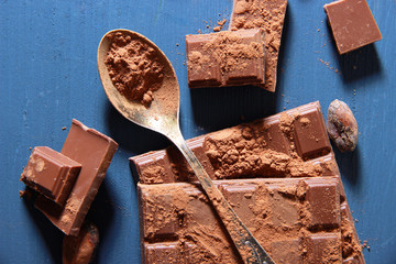 Cocoa powder and dark chocolate on color wooden background