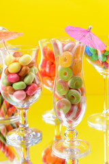 Different colorful fruit candy in glasses on yellow background