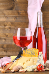 Pink wine and different kinds of cheese on wooden background