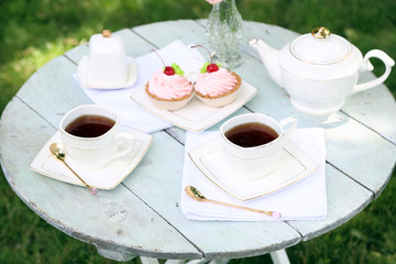 Coffee table with teacups and tasty cakes in garden