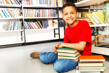 Smiling schoolchild with pile of books on floor