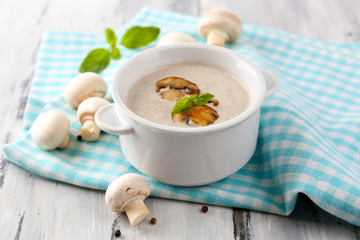 Mushroom soup in white pot, on napkin,  on wooden background