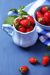 Ripe sweet strawberries in mugs  on color wooden background