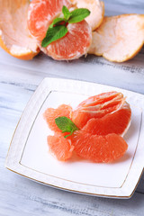 Ripe peeled grapefruits on plate, on color wooden background