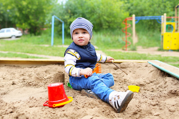 baby playing with sand on playground in summer