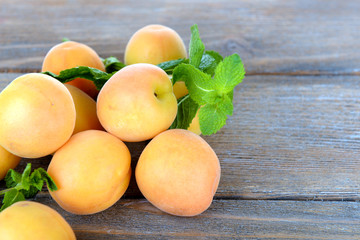 Ripe apricots with green mint leaves on wooden background