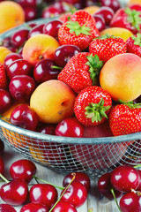 fresh berries and fruits in metallic basket on wooden surface