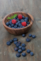 wooden bowl with blueberries and raspberries, vertical
