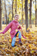 Little girl runs along autumn park kicking up fallen leaves