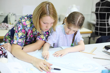 Female tailor teaches student girl how to draw patterns