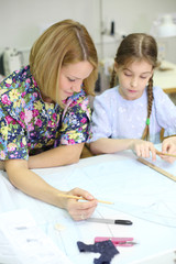 Smiling female tailor and student girl draw patterns for clothes