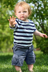 Little barefoot boy in shorts stands on green grass