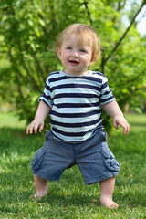 Little barefoot boy in striped T-shirt stands on grass
