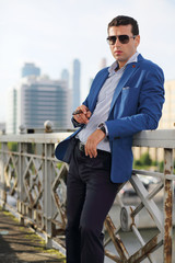 Handsome man in jacket and sunglasses with cigar stands