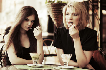 Two young women eating an ice cream at sidewalk cafe