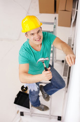 smiling man in helmet hammering nail in wall