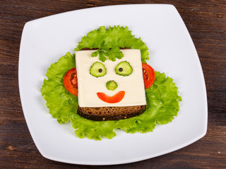 Face on bread, made from cheese, lettuce, tomato, cucumber