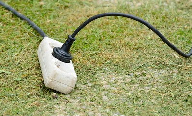Old white plastic extension adapter plug cable at garden.