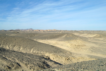 Egyptian desert covered by black stones and blue sky.